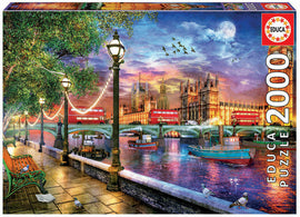 A colorful jigsaw puzzle box featuring a scenic view of London at sunset. The image shows the iconic Big Ben and Westminster Palace illuminated by the setting sun, with red double-decker buses, boats on the river, and a charming riverside park with trees and lampposts. The puzzle consists of 2000 pieces and is made by Educa.