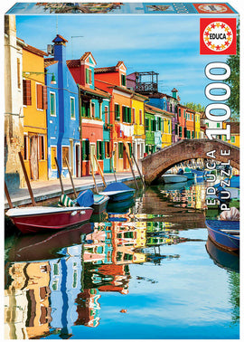 Burano jigsaw puzzle by Educa featuring a colorful canal scene with vibrant houses reflecting in the water, showcasing a picturesque view of Burano, Italy. The puzzle contains 1000 pieces, perfect for both beginners and experienced puzzlers.