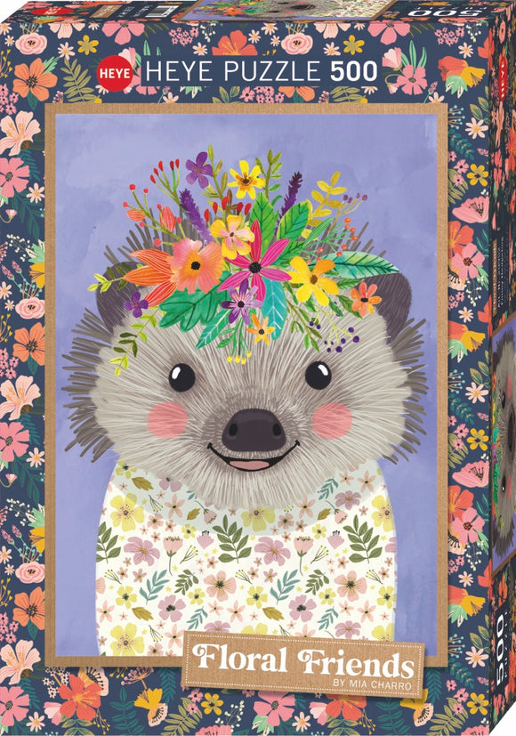 A colorful jigsaw puzzle box featuring a cute hedgehog with a floral crown. The hedgehog has a happy expression, with pink cheeks and is wearing a flower-patterned shirt. The background is a soft purple, adorned with vibrant floral motifs framing the hedgehog.