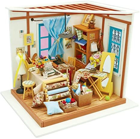 A detailed diorama of a tailor's workshop, featuring a variety of miniature furnishings and sewing materials. The scene includes a wooden table with fabric rolls, a sewing machine, colorful spools, and decorated walls with framed pictures. Brightly colored curtains and a cozy ambiance create a vibrant atmosphere for creative crafting.