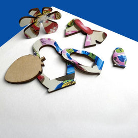 A colorful jigsaw puzzle featuring intricately designed pieces shaped like nesting dolls. The pieces display vibrant floral patterns and are made from wood, showcasing a mix of playful colors including pink, blue, and green. The puzzle pieces are arranged on a light-colored surface, highlighting their detailed artwork and craftsmanship.