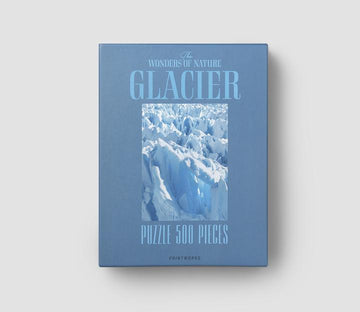 The Glacier Puzzle by Printworks is a 500-piece jigsaw puzzle featuring a stunning image of a blue glacier. The box is a soft blue color with the title 'Glacier Puzzle 500 Pieces' prominently displayed. This puzzle is part of 'The Wonders of Nature' series and is designed to provide a challenging and visually engaging experience for puzzle enthusiasts.