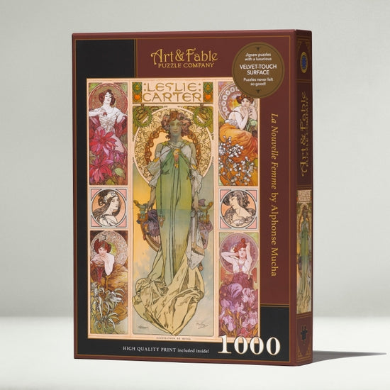Art & Fable Puzzle Company's 'La Nouvelle Femme' jigsaw puzzle featuring elegant illustrations by Alphonse Mucha. The box showcases the intricate design, including lush floral patterns and artistic depictions of women, promising a high-quality 1000-piece experience with a velvet touch surface.