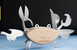 A whimsical Crab Multi Tool by Kikkerland with various stainless steel tools integrated into a crab design, including scissors, a screwdriver, and other utility functions, all set against a simple dark background. The body's surface has a natural wood finish, adding a unique touch.