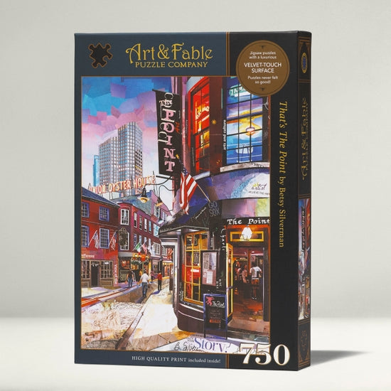 Packaging for the Art & Fable Puzzle Co. jigsaw puzzle titled 'That's The Point,' featuring vibrant artwork of a street scene with the sign for 'The Point' prominently displayed. The box includes indications of its quality, including the Velvetouch surface and that it consists of 750 pieces.