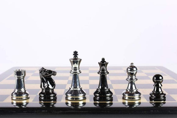 A close-up view of metal chess pieces inspired by Bobby Fischer, featuring a variety of styles including a shiny black knight, metallic bishop, queen, king, rook, and pawn arranged neatly on a chessboard. The set is designed by Wood Expressions, showcasing the elegance and sophistication of traditional chess games.