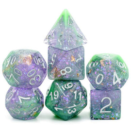 A vibrant Green & Purple Seabed Treasure RPG Dice Set from Foam Brain Games, featuring a variety of dice including a d20, d12, d10, d8, d6, and d4. The dice are semi-transparent with a swirled pattern of green and purple colors, sprinkled with gold flecks, offering a unique and eye-catching design perfect for tabletop gaming.