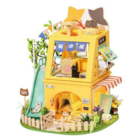 A colorful, detailed miniature cat house designed by Robotime. The DIY kit features multiple levels, complete with a slide, scratching posts, and playful cat figurines. The house is surrounded by greenery and includes charming decorations like flower pots and a cute sign that says 'Cat'. Ideal for crafting enthusiasts and cat lovers alike.