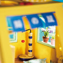 A brightly colored miniature cat house from Robotime, showcasing an engaging interior view with a colorful scratching post, a hanging toy, and window plants. This DIY kit features intricate details, making it a perfect project for cat lovers and miniature enthusiasts.