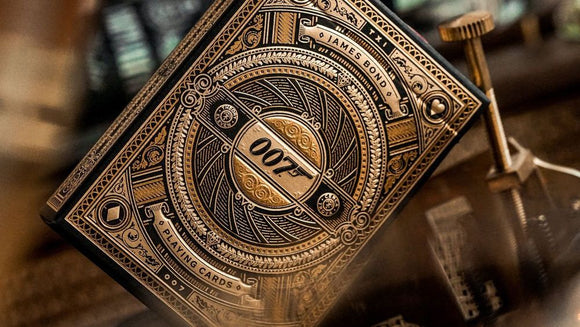 James Bond 007 playing card deck by Theory 11, featuring intricate gold and black designs. The card box displays the iconic 007 logo and decorative elements, emphasizing a high-quality collectible for card game enthusiasts.