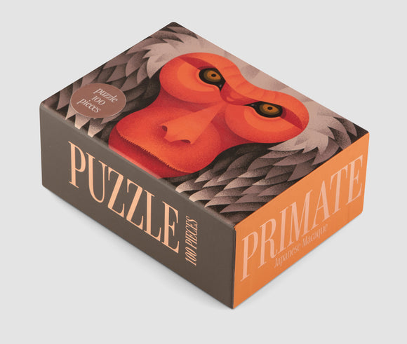 The Japanese Macaque 100-piece jigsaw puzzle by Printworks features a colorful, stylized illustration of a primate's face on the box. The design includes bold colors and striking facial features, appealing to puzzle enthusiasts and animal lovers alike.