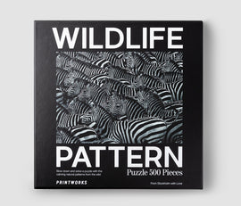 Wildlife Pattern Zebra jigsaw puzzle featuring an intricate design of numerous zebras with striking black and white stripes. The box design includes the words 'WILDLIFE' and 'PATTERN' in bold white letters against a black background, with the text indicating it is a 500-piece puzzle. The packaging is designed by Printworks, suggesting a calming and engaging jigsaw experience.