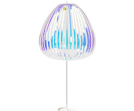 The Rainbow Stick Deluxe by Prodia is a vibrant, translucent lamp featuring a unique design with colorful vertical strips of varying widths. Its modern shape resembles a jellyfish or a blooming flower, casting a playful glow in any environment, making it a perfect decorative and ambient lighting piece.