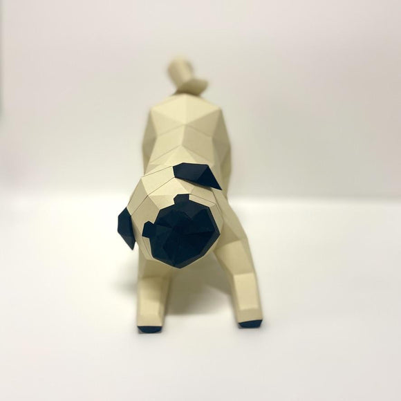 A 3D crafted model of a pug made from low poly materials. The pug is depicted in a playful pose, featuring geometric shapes and a beige color palette with dark accents on the face and paws. It stands on a white background, emphasizing its unique design.