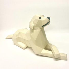 A low poly craft model of a retriever laying down, made of geometric shapes in a cream color. The model showcases a relaxed posture, with defined features and an artistic design, perfect for DIY enthusiasts or home decor.
