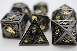 A Hollow Night Dragon Metal RPG Dice Set featuring intricately designed black dice with gold numbering. The set includes various polyhedral shapes, such as d4, d6, d8, d10, d12, and d20, ideal for tabletop role-playing games, showcasing detailed dragon motifs carved into the surface.