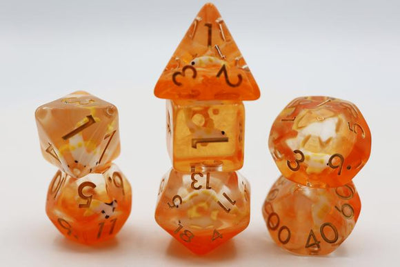 A vibrant Golden Koi Fish RPG Dice Set by Foam Brain. The dice are a mix of orange and yellow translucent resin with black numbering, showcasing a d20, d12, d10, d8, d6, and d4, beautifully stacked with intricate details reflecting light.