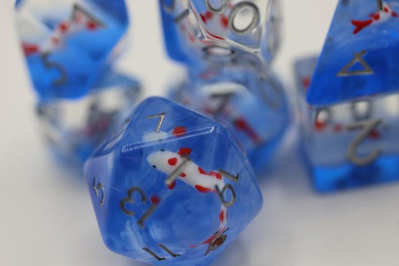 A vibrant Koi Pond RPG Dice Set featuring translucent blue dice with colorful koi fish designs inside, showcasing various numbers in elegant gold printing. The set includes multiple dice shapes designed for role-playing games, perfect for adding a unique touch to any gaming session.