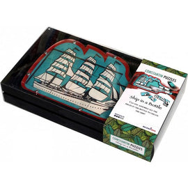A close-up view of the Constantin Puzzles 'Ship in a Bottle' mechanical puzzle. The puzzle features intricate details of a vintage ship design on a vibrant blue background, encased in a sleek black box. The packaging showcases the product name and a challenge description, enticing users to assemble the pieces to create the ship.