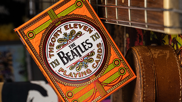 A close-up image of a vibrant orange playing card box featuring The Beatles and Theory 11 branding. The intricate design showcases colorful artistic details and text, set against a textured background