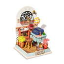 The Record Mood Study Model Kit by Robotime features a miniature workspace adorned with vibrant plants, a vintage typewriter, and decorative elements like a cheerful 'Lucky' sign and colorful balloons. The intricate details create a charming environment, making it perfect for DIY enthusiasts and collectors of unique models.