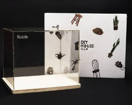 A Robotime Acrylic Cover Medium DIY kit displayed with its packaging. The acrylic cover features a clear, transparent design and is set on a wooden base. The packaging showcases colorful, whimsical illustrations of furniture and plants, emphasizing a creative, hands-on experience.