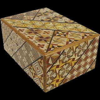 A beautifully crafted mechanical puzzle box with intricate geometric patterns and designs in various colors. The box is closed, showcasing its unique artistry, featuring stars, triangles, and other shapes across its surface.