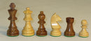 A collection of six chess pieces including a 3-inch king made of acacia wood and boxwood. The set features intricately designed pieces, highlighting the craftsmanship and quality materials used. The chess pieces are displayed in a line on a neutral background, showcasing the contrasting colors of the wood.
