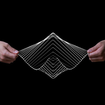 A person is holding the Square Wave Silver, a unique, interactive fidget toy made of flexible wire, forming a geometric, three-dimensional wave shape. The toy's intricate design allows for mesmerizing motion and manipulation, providing a soothing tactile experience.