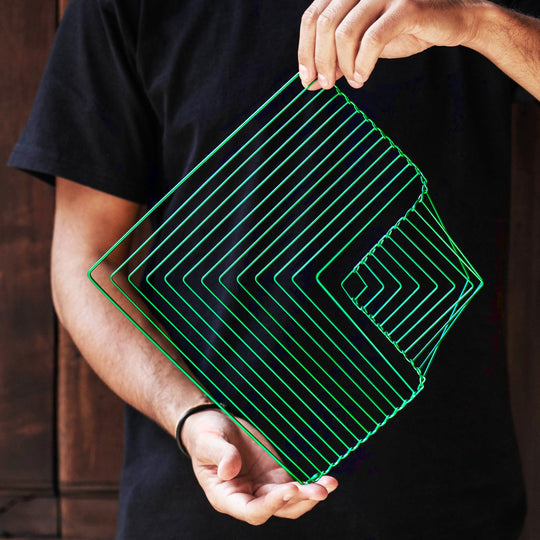 A person holding a square wave-shaped puzzle in emerald green, designed with multiple layers that create a unique visual pattern. The puzzle is crafted from sturdy material and showcases a modern geometric design, perfect for both decoration and entertainment.