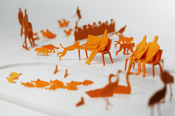 A set of intricately crafted orange paper figures depicting a zoo scene. Various animal shapes like cats, birds, and a group of people sitting on benches, creating a playful and artistic representation of a zoo environment.