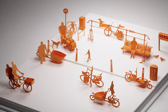 The Amsterdam Model by TERADA MOKEI is a detailed DIY kit featuring orange paper cutouts of various urban scenes. The model includes bicycles, pedestrians, benches, and traffic signals, arranged on a white backdrop to mimic the vibrancy of city life in Amsterdam. Each element is intricately designed for enthusiasts of architectural and urban design.