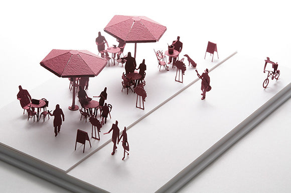 A detailed Open-air Cafe model made by TERADA MOKEI, featuring pink paper figures seated at tables under umbrellas, capturing a lively cafe atmosphere with pedestrians and a cyclist.