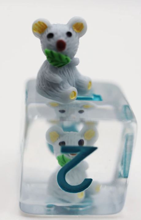 Close-up of the Koala RPG Dice Set by Foam Brain, featuring a cute koala figurine atop a clear die. The die shows a blue number '2' with a sitting koala underneath, highlighting the playful design perfect for tabletop role-playing games.