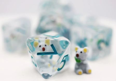 A colorful Koala RPG Dice Set featuring translucent polyhedral dice with turquoise numbers. A small, adorable koala figure accompanies the dice, enhancing the playful theme of the set. Ideal for tabletop role-playing games, these dice provide both functionality and charm.
