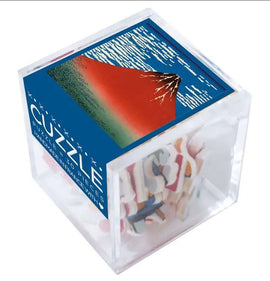 A jigsaw puzzle titled 'THE RED FUJI' by Wilson Jeux, presented in a clear cube packaging. The top features a vibrant illustration of Mount Fuji against a blue sky with stylized clouds, while the sides reveal colorful puzzle pieces inside.