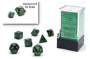 A set of seven jade and gold polyhedral dice from Chessex, featuring various shapes including a pyramid, cube, and more. A standard d10 is shown for scale. The dice are displayed in a clear packaging box with a black base.