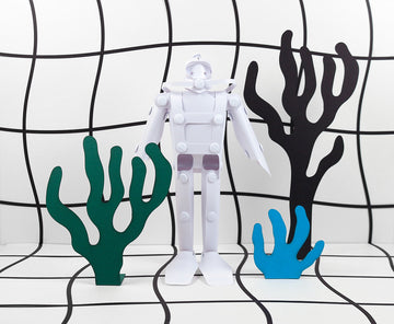 A DIY model kit featuring a white diver figure with movable joints, accompanied by colorful coral shapes in green and blue. The diver stands on a grid-patterned background, adding a playful touch to the scene.