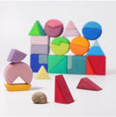 A colorful building set featuring various geometric shapes including triangles, squares, and circles made by Grimm's. The pieces are arranged in stacks and formations, showcasing vibrant colors like pink, blue, green, yellow, and red. A small snail is placed in the foreground next to some of the shapes, emphasizing the playful nature of this educational toy.