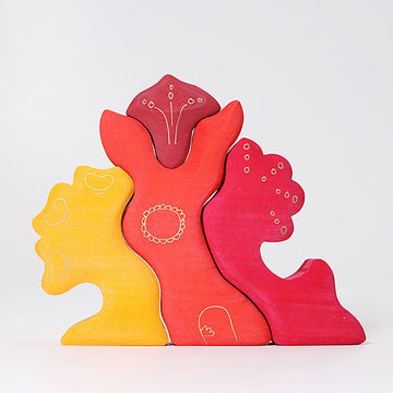 Casa Glora by Grimm's features vibrant, hand-painted wooden pieces shaped like various abstract forms in shades of red, yellow, and pink, designed for imaginative play and creativity. Each piece showcases unique engravings, adding an artistic touch to this versatile toy that encourages open-ended exploration and construction.