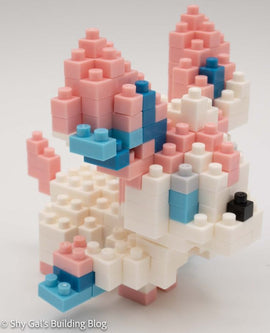 A detailed view of the Nanoblock Sylveon DIY kit featuring colorful interlocking blocks. The Sylveon figure is composed of pink, white, and blue blocks, showcasing its signature ear shapes and delicate features, perfect for creative building enthusiasts.