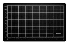A black cutting mat measuring 5.5 inches by 9 inches, featuring a grid pattern with white lines and measurement markings along the edges, ideal for precise cutting and crafting.