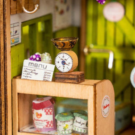 Detailed wooden model kit of a sweet jam shop featuring a miniature scale, colorful jars of jam, and a menu board, perfect for DIY enthusiasts and crafters.