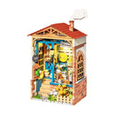 The Dream Yard Model Kit by Robotime showcases a charming miniature cottage with detailed features, including a welcoming front door, colorful potted plants, and a classic red-tiled roof. The intricate design captures a cozy outdoor setting, perfect for DIY enthusiasts.