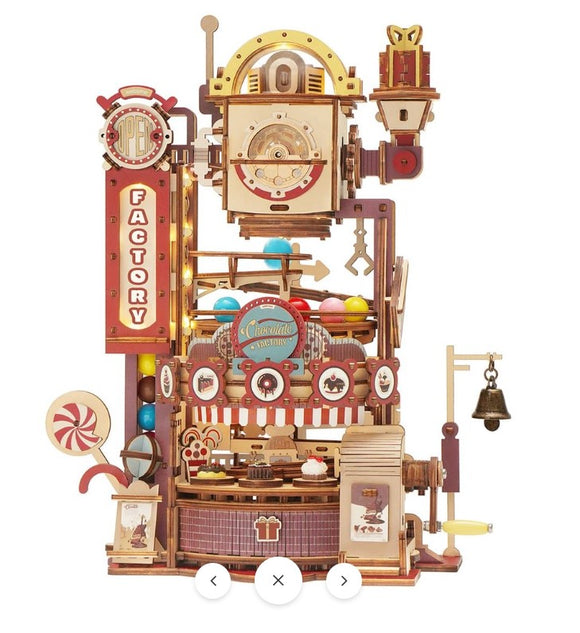 A detailed Chocolate Factory Marble Run Model Kit by Robotime, featuring intricate wooden components, colorful balls rolling through a mechanical system, candy-themed decorations, and a small bell. This DIY kit presents a whimsical and playful design, ideal for creativity and hands-on fun.