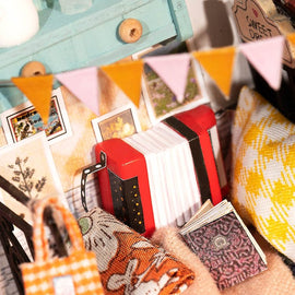 The Sweet Dreams Bedroom Model Kit by Robotime features a cozy miniature scene with colorful cushions, an accordion, and decorative items like a book and bunting. The intricately designed pieces reflect a whimsical and inviting atmosphere, perfect for DIY enthusiasts looking to create their own charming bedroom setting.
