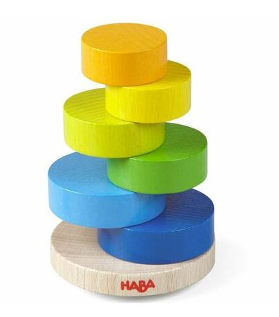 The Stacking Game Wobbly Tower by Haba features a colorful arrangement of six wooden discs in bright shades of yellow, green, and blue. The discs are stacked on a sturdy circular base, promoting hand-eye coordination and fine motor skills in children. This engaging toy encourages imaginative play and helps develop essential skills in a fun way.
