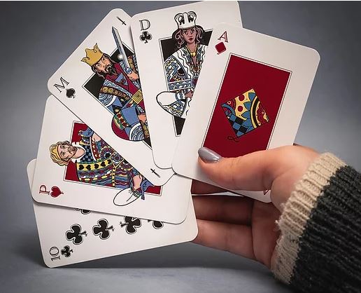A hand holding five red standard playing cards featuring colorful illustrations of the King, Queen, and Jack from various suits. The cards include the Ace of Diamonds, Queen of Spades, King of Hearts, and 10 of Clubs, displaying a vibrant design that enhances gameplay.