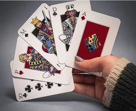 A hand holding five red standard playing cards featuring colorful illustrations of the King, Queen, and Jack from various suits. The cards include the Ace of Diamonds, Queen of Spades, King of Hearts, and 10 of Clubs, displaying a vibrant design that enhances gameplay.