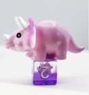 A playful pink Triceratops dice set from Foam Brain Games featuring a cute, stylized dinosaur figure on top of a purple die. The dice set is ideal for tabletop role-playing games, combining whimsy and functionality for a fun gaming experience.